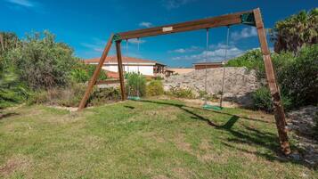 A wooden swing set in a grassy yard with a house in the background.