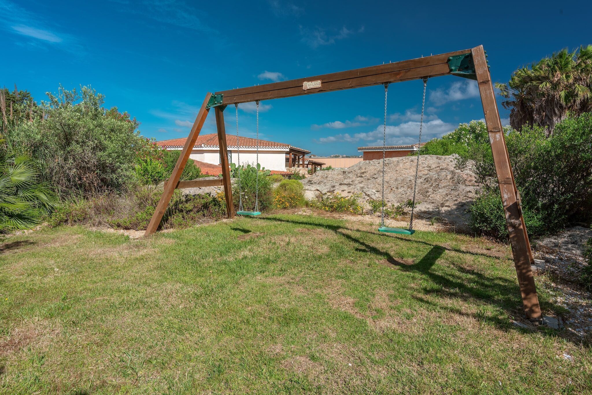 A wooden swing set in a grassy yard with a house in the background.