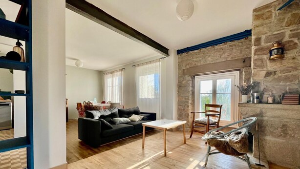 A spacious living area with a black sofa, a wooden coffee table, and a stone fireplace. - L'Authentik (Gouesnach)