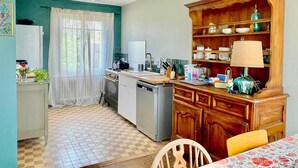 A compact kitchen with a sink, stove, and cabinets. There is a dining table with chairs and a window with curtains. - L'Authentik (Gouesnach)