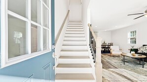 Eine Treppe mit weißen Stufen und Holitzerhandläufen führt zu einem Raum mit einem Essbereich, einer Couch und einem Couchtisch.