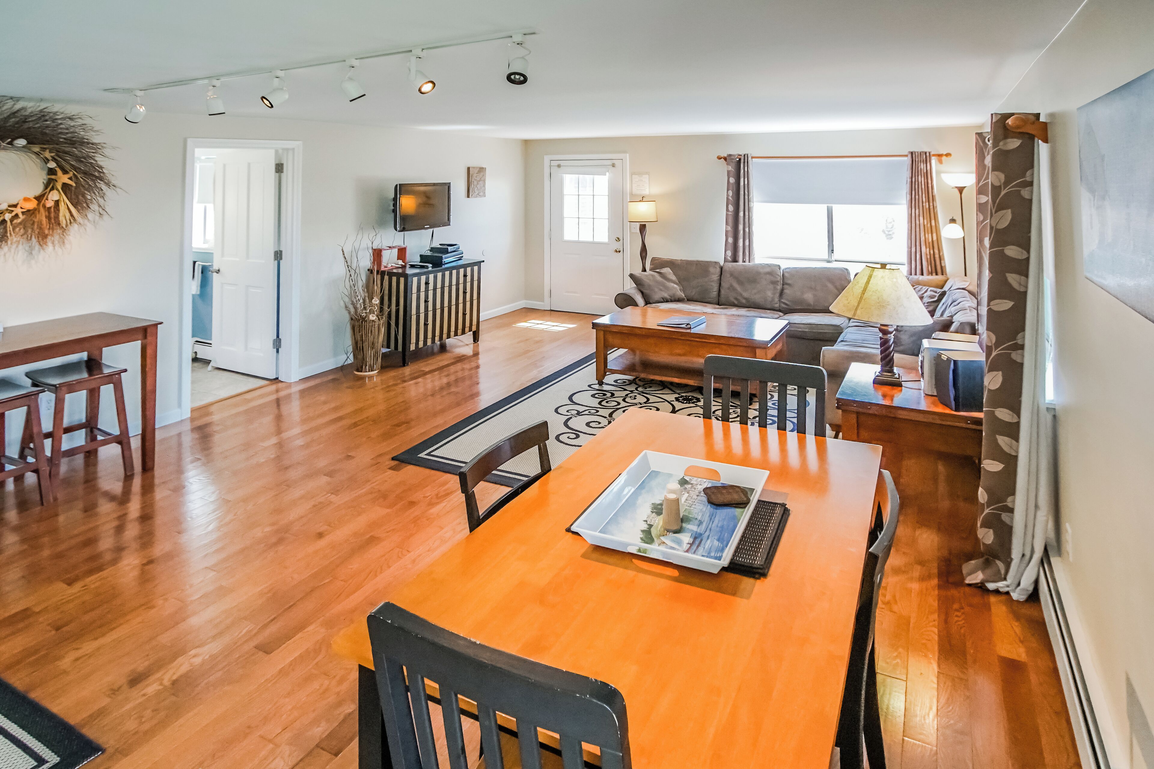 A spacious living area with a wooden dining table, a sofa, and a TV.