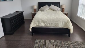 A bedroom with a bed, nightstands, a dresser, and a painting on the wall.