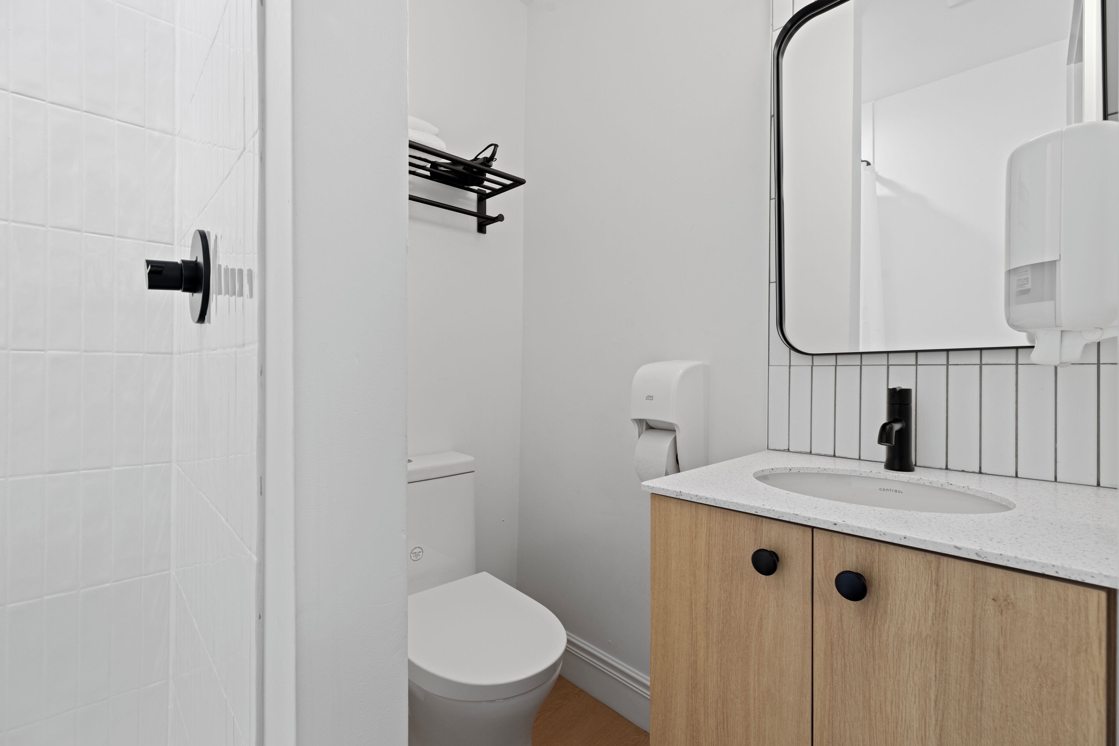 A modern bathroom with a white toilet, a sink with a mirror, and a soap dispenser.