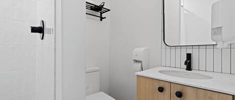 A modern bathroom with a white toilet, a sink with a mirror, and a soap dispenser.