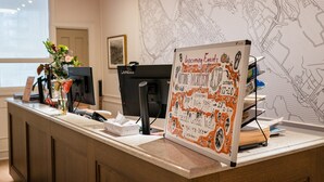 A reception desk with a whiteboard listing upcoming events, a computer, and a map on the wall. - HI Halifax Heritage House - Hostel (Halifax)