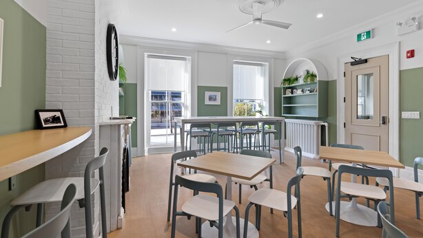 A modern dining area with white brick walls, green accents, and a ceiling fan. Tables and chairs are arranged for dining. - HI Halifax Heritage House - Hostel (Halifax)