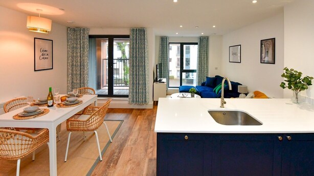 Eine moderne Küche mit Kochinsel, Essbereich mit Korbstühlen und ein Wohnzimmer mit blauem Sofa.
