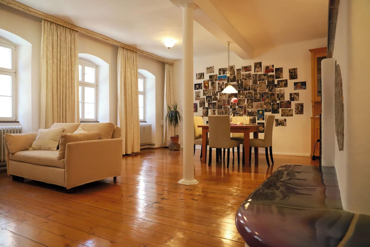 A spacious living room with a wooden floor, a beige sofa, a dark-colored couch, and a dining area with a table and chairs.