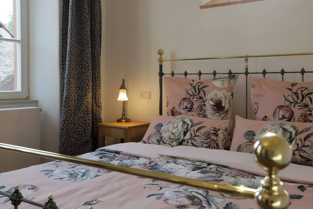 A neatly made bed with floral bedding, a bedside lamp, and a window with curtains.