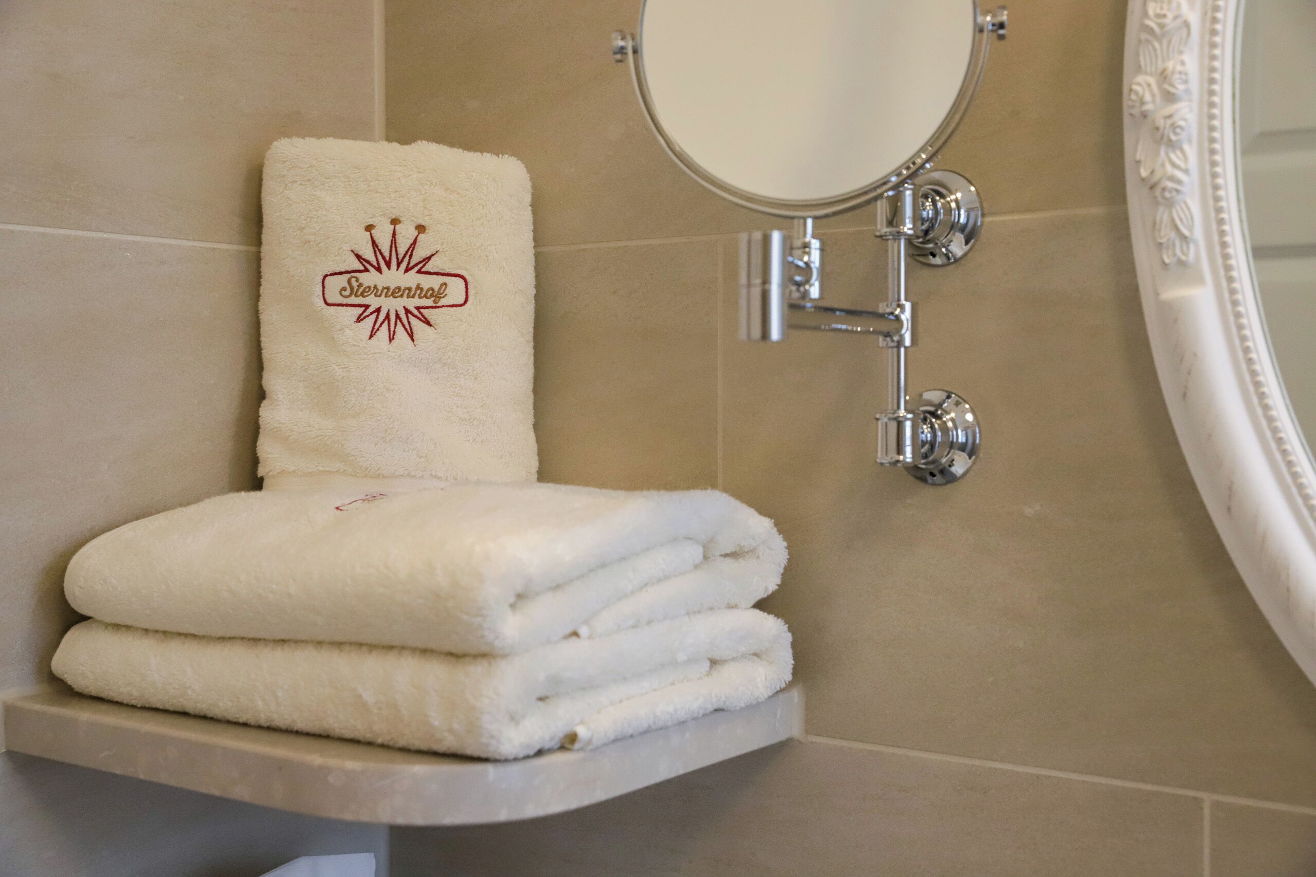 A bathroom with a towel rack holding a folded towel and a towel with a logo.