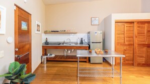 Cocina compacta con piso de madera, pileta de acero inoxidable, refrigerador y una pequeña mesa con estante metálico.