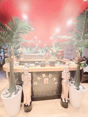 A bar area with a counter, two palm trees, and a statue of a figure. - OYO Kingswood Hotel (Maidenhead)