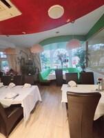 A restaurant with tables set for dining, a green sofa, and large windows with a view of the outside.