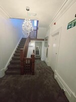 A staircase with a chandelier, a fire exit sign, and a door with a number.