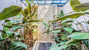 Een stenen muur met een glazen constructie erboven, omgeven door weelderige tropische planten.