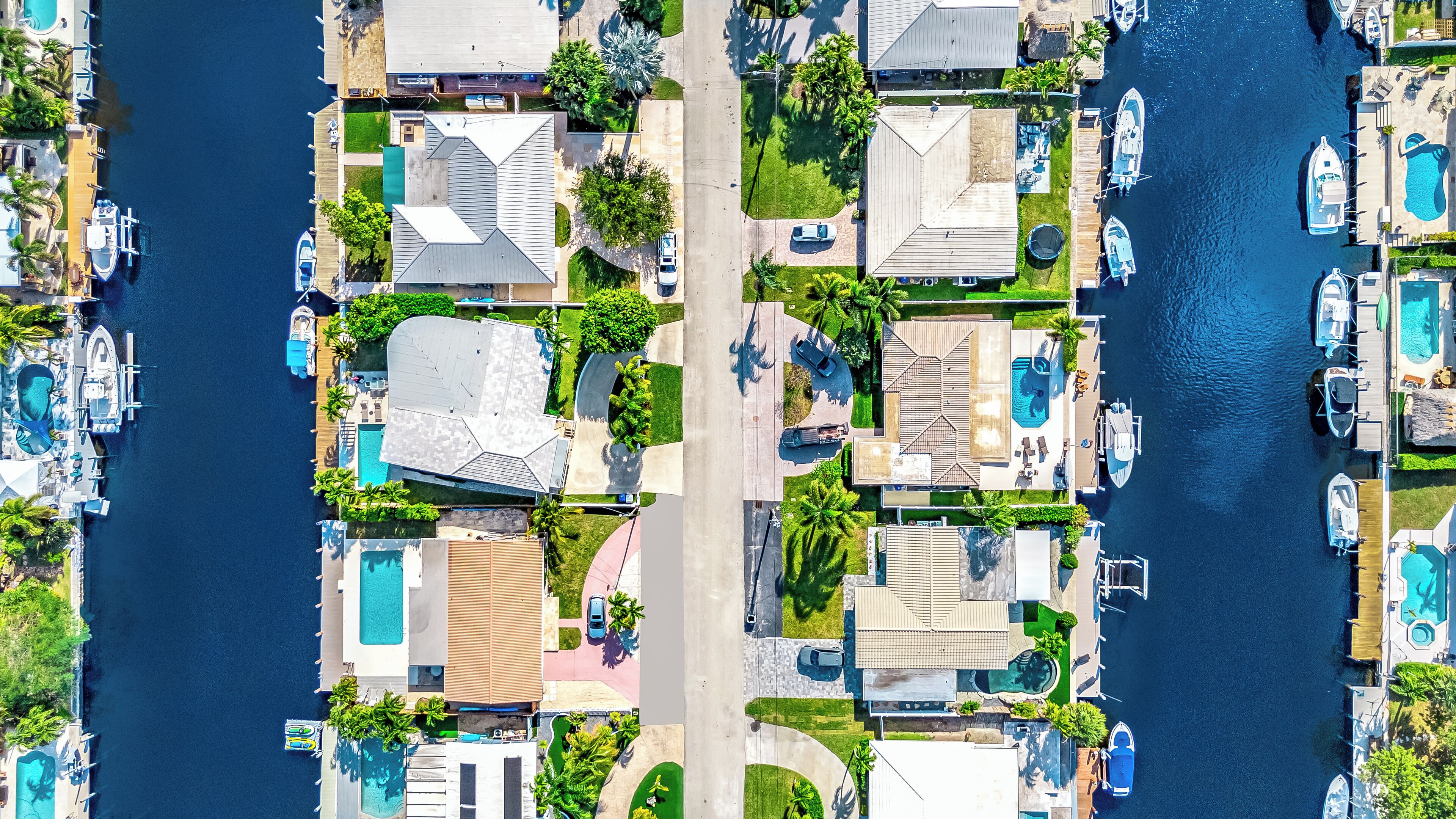 Vista aérea de una zona residencial costera con varias casas, cada una con piscina, muelle y embarcaciones, además de abundante vegetación.