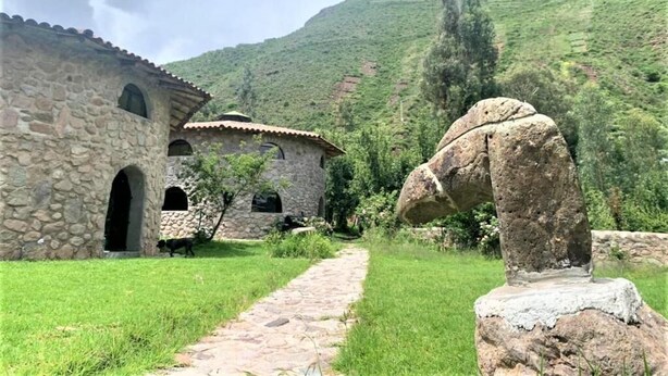 A stone building with a tiled roof, a stone pathway, and a large rock formation. - ILLA WASI SACRED VALLEY - BUNGALLOW 3 ROOMS (Urubamba)