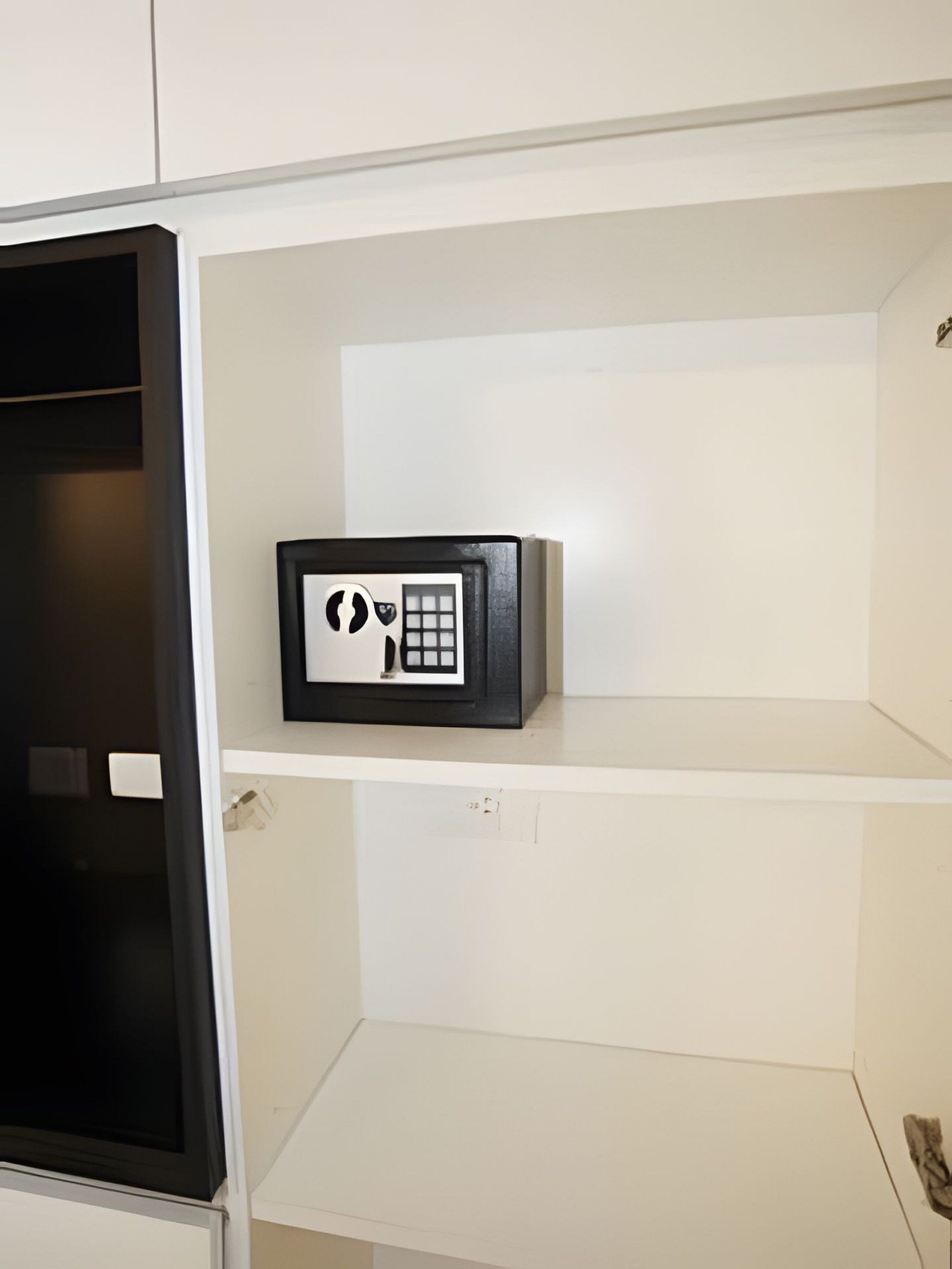 A room with a white wardrobe, a black-framed mirror, and a white shelf with a black object.