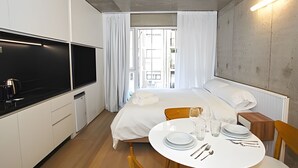 Quarto de hotel pequeno com uma cama, uma mesinha de jantar posta com pratos, copos e talheres, uma televisão e uma janela com cortinas.