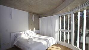 Une chambre avec un grand lit, des rideaux blancs et une vue par les fenêtres.