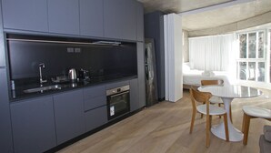 Une cuisine moderne avec des armoires grises, un réfrigérateur en acier inoxydable et un four encastré. On y trouve également un coin repas avec une table ronde et des chaises en bois.
