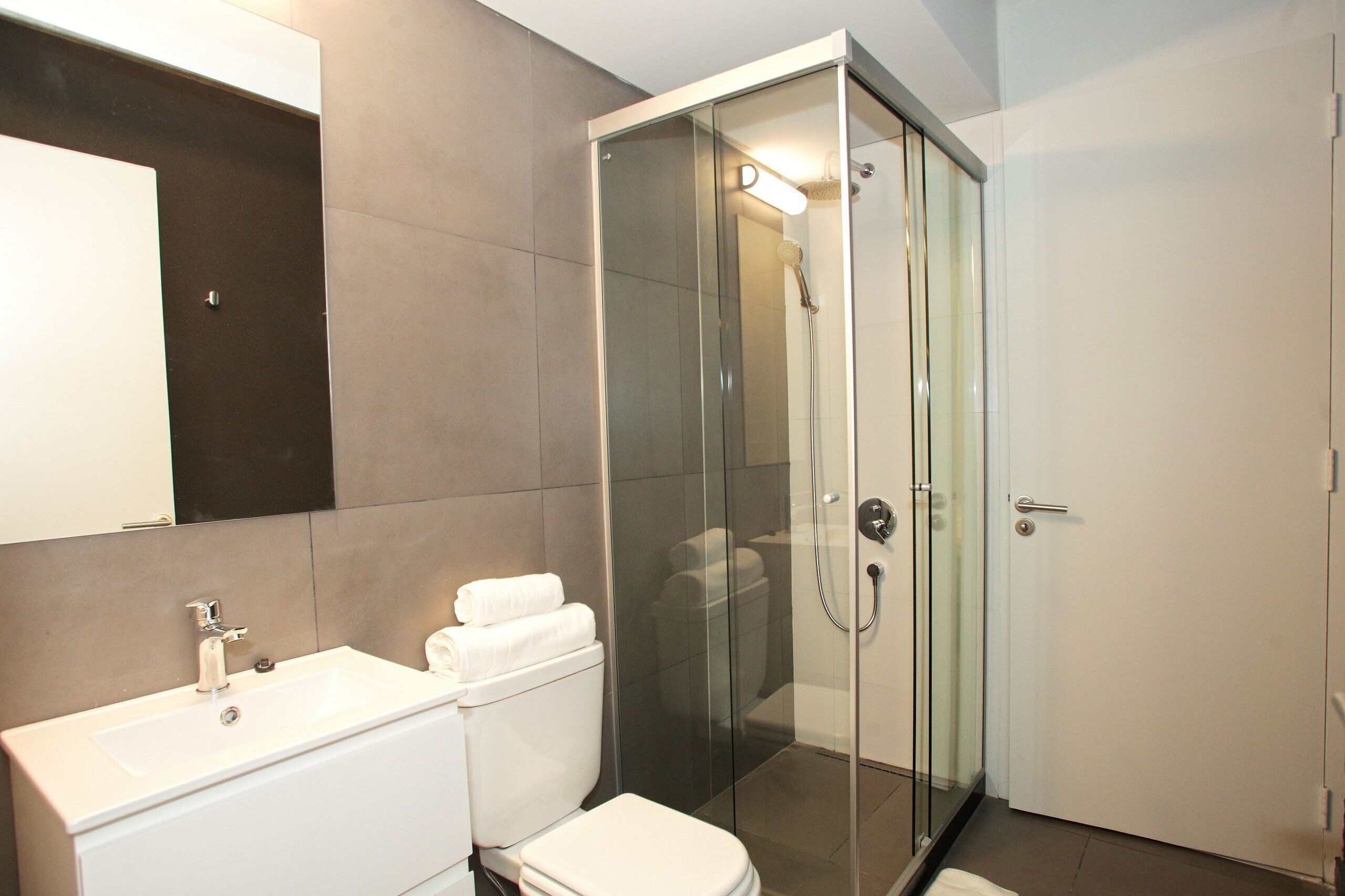 A modern bathroom with a glass-enclosed shower, a white sink, and a toilet.