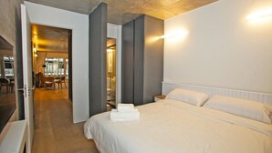 Une chambre d’hôtel avec un grand lit, un plancher en bois, une salle de bain avec une porte en verre et un coin repas comprenant des chaises et une table.