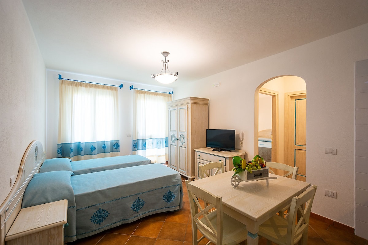 Ein Zimmer mit zwei Betten, einem Fernseher, einem Esstisch und einer Küchenzeile.