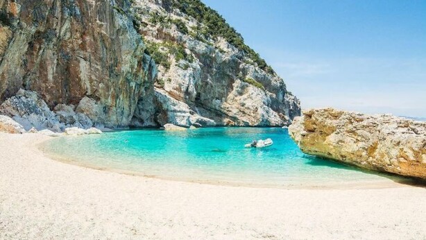 Uma praia com águas turquesa cristalinas, areia branca e falésias rochosas.