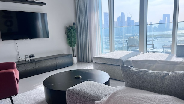 A modern living room with a large window, a flat-screen TV, a grey sofa, a red chair, and a black coffee table.