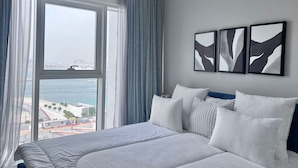 A modern hotel room with a large bed, a view of the sea, and abstract art on the wall.