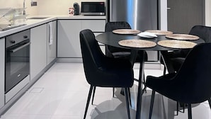 A modern kitchen with a stainless steel refrigerator, black chairs around a dining table, and a microwave on the counter.