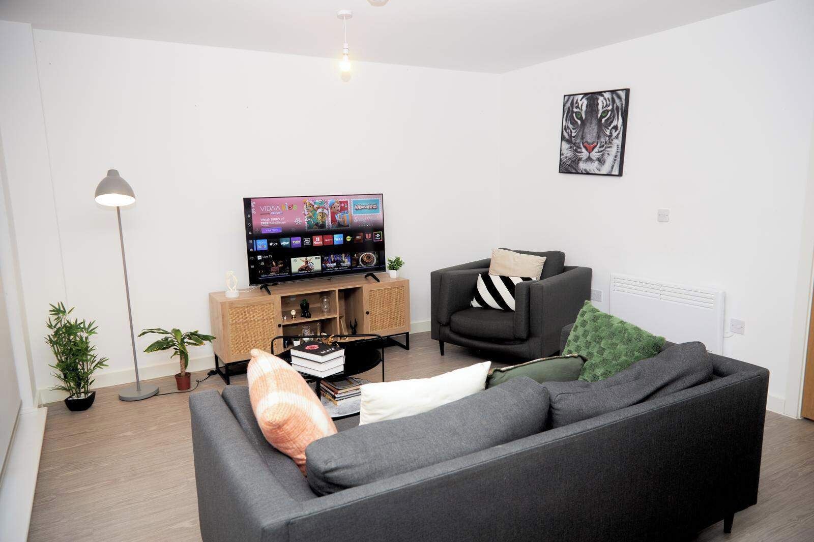 Una sala de estar moderna con un sofá gris, un sillón negro, un televisor sobre un mueble de madera y una planta verde.