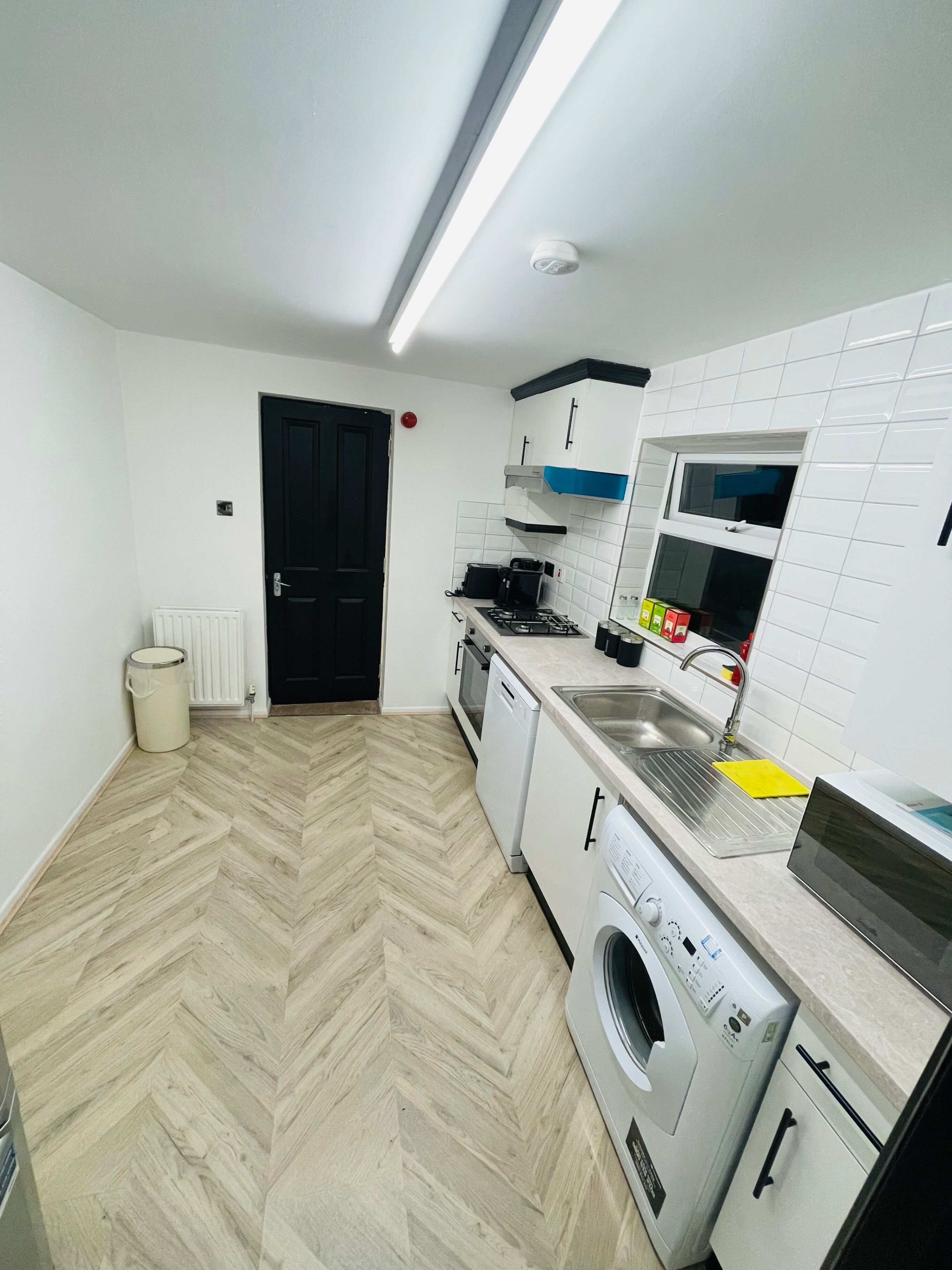 Eine moderne Küche mit Fischgrätparkett, weißen Schränken, einem Backofen, einem Geschirrspüler und einem großen Fenster über der Spüle.