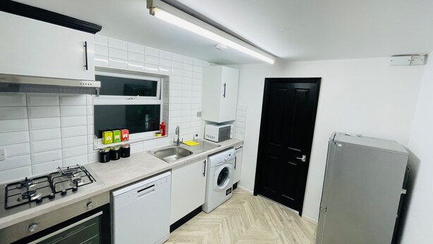 Une cuisine compacte avec des meubles blancs, un four à micro-ondes, un évier, une cuisinière, un lave-vaisselle, une machine à laver et un réfrig érateur.