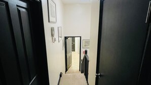 Un couloir étroit, dont le sol est recouvert de moquette, avec des portes noires de chaque côté et un luminaire au plafond.