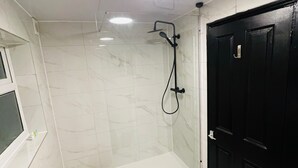 Une salle de bain avec une douche, une porte noire et une fenêtre.