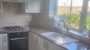 A kitchen with white cabinets, a gas stove, an oven, a sink, and a window with a view of greenery. - Charming Home in Huddersfield w/ Parking Petsok (Huddersfield)