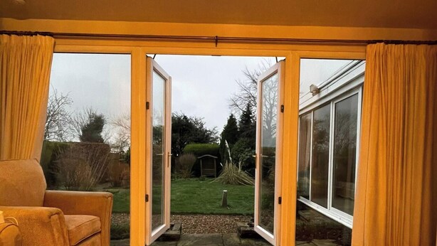 A room with a wooden floor, a sofa, and a sliding glass door leading to a garden. - Charming Home in Huddersfield w/ Parking Petsok (Huddersfield)