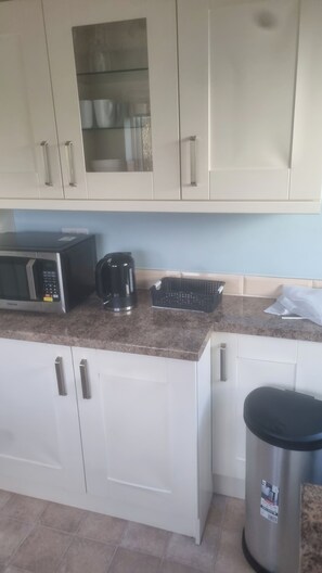 A kitchen with white cabinets, a microwave, a coffee maker, and a trash bin. - Charming Home in Huddersfield w/ Parking Petsok (Huddersfield)