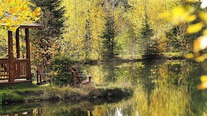 Un quiosco de madera junto a un lago tranquilo rodeado de follaje otoñal.