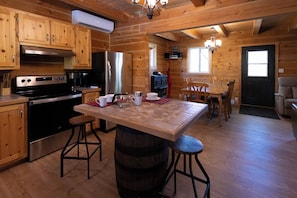 A wooden cabin kitchen with a central island, bar stools, a stove, refrigerator, and a dining table with chairs.