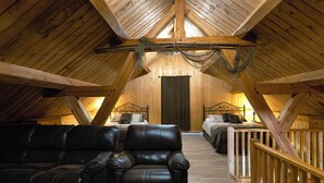 Un dormitorio en el ático con una cama elevada, un sofá de cuero y una barandilla de madera.
