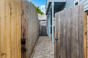 A narrow wooden pathway leading to a building with a blue exterior and a visible staircase.