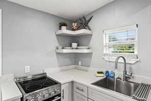 A kitchen with a stove, sink, and white countertops.