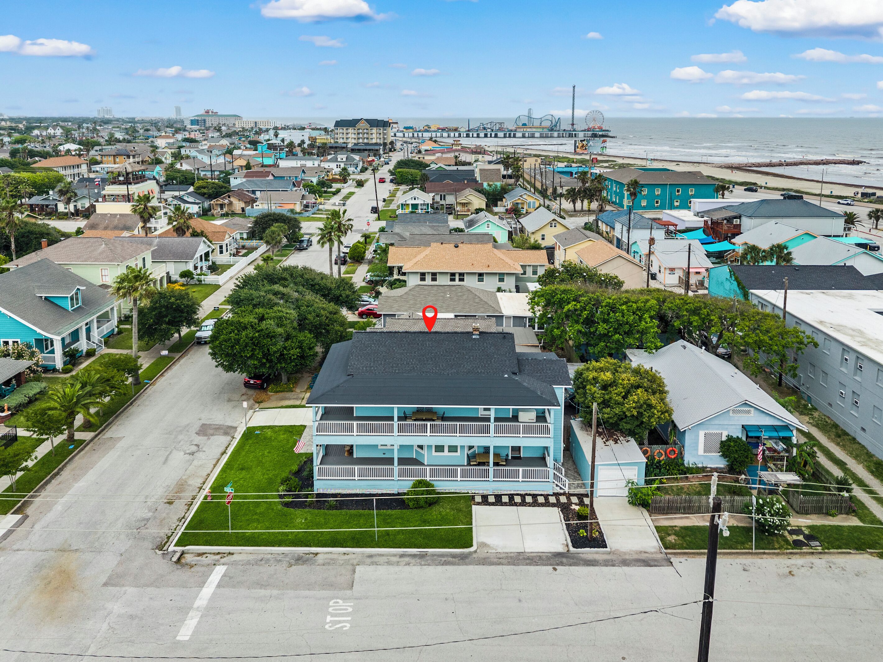 Uma cidade costeira com um edifício azul imponente e varanda, cercada por casas residenciais e um cais ao fundo.