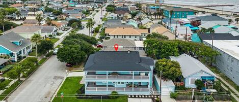 Uma cidade costeira com um edifício azul imponente e varanda, cercada por casas residenciais e um cais ao fundo.