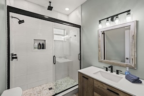 A modern bathroom with a glass-enclosed shower, a white sink with a mirror above, and a wooden vanity. - The Lookout at R½ | Hot Tub • Sauna • Wraparound Deck • Steps to Beach (Galveston)