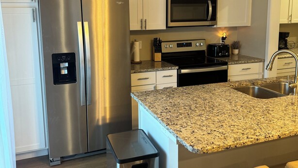 A modern kitchen with white cabinets, stainless steel appliances, granite countertops, and a small trash bin.
